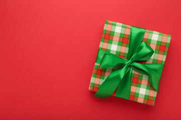 A green gift with green ribbon on red background. Space for text