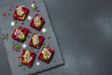 Fototapeta na wymiar A delicious festive appetizer with herring on pieces of beet waffles with spices and sauce