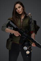 Fototapeta na wymiar Middle Eastern-looking woman dressed in survivalist clothing posing with a rifle against a gray background, portraying strength and resilience