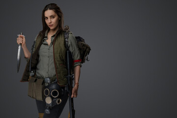 Middle Eastern descent in post-apocalyptic survival gear, brandishing a dagger on a gray backdrop,...