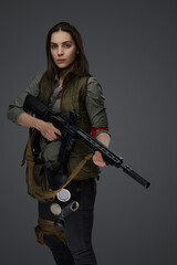 Middle Eastern-looking woman dressed in survivalist clothing posing with a rifle against a gray background, portraying strength and resilience