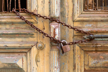 Rusty padlock and chain on an wooden closed entrance door closeup.