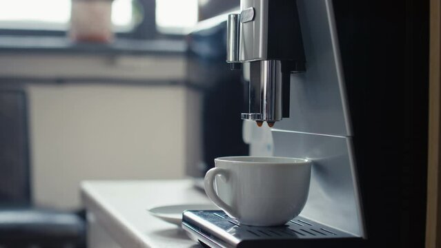 Midsection side shot of coffee machine filling cup with latte or cappuccino and unrecognizable office worker taking cup in office