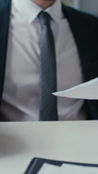 Vertical closeup shot of hands of unrecognizable businessman stapling paperwork during work in office