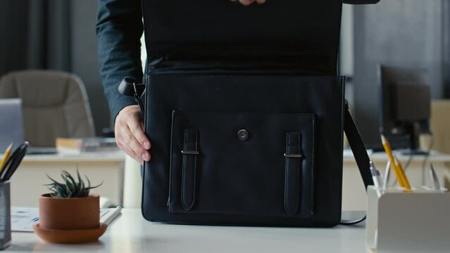 Cropped shot of unrecognizable businessman in suit coming up to desk, opening briefcase and taking out necessary items for work in cozy office