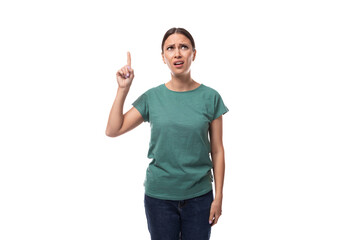 Fototapeta premium 30 year old slender brunette woman with collected hair dressed in a green basic t-shirt works as a promoter and points with her hand at an empty space for advertising