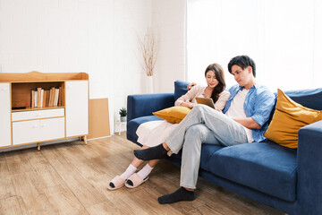 An attractive married man holding a tablet and a woman sit on the floor together in the living room looking at the camera at the new home. A family spends quality time together after home moving.