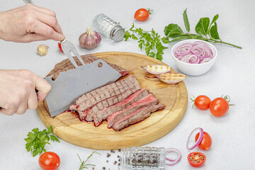 Woman cuts grilled steak. Female hands with knife and two pronged fork. Fresh herbs, vegetables