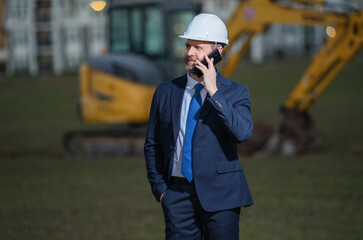 Construction manager in suit and helmet at a construction site. Construction manager worker or supervisor wearing hardhat in front of house. Supervisor construction manager near excavator. Renovation.