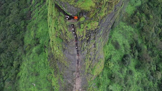 Drone shot of ancient Harihar Fort with tourists climbing down steep and vertical stairs during monsoon trek, Harshewadi, Nashik, Maharashtra, India