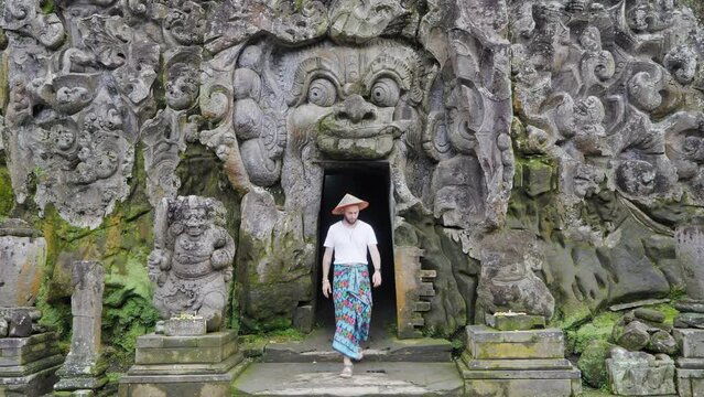 Journey into Mystery: Male Tourist dressed in traditional Balinese Sarong Explores Goa Gajah Elephant Cave, one of the holiest temples in Ubud, Bali. 4K Footage: Ideal for Spiritual and travel videos