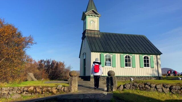 Female tourist approaching Icelandic fairytale church in Thingvellir at sunny day