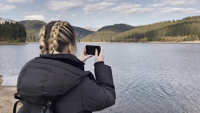 Woman With A Mobile Phone Taking A Picture Of Bolboci Lake In Romania. Close Up