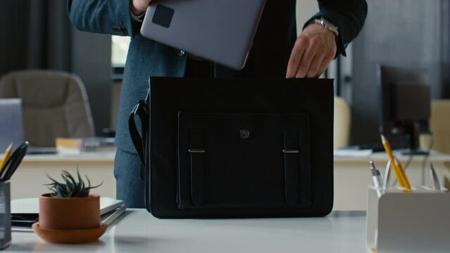 Cropped shot of unrecognisable businessman packing laptop and paperwork into briefcase and leaving office