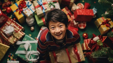 A happy Asian boy with lots of Christmas presents or gifts around him, looking at a camera, aerial view, Xmas hoiday and celebration..