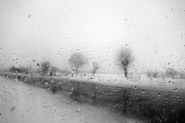 View on winter road and trees through wet windshield with rain drops. Black and white - obrazy, fototapety, plakaty