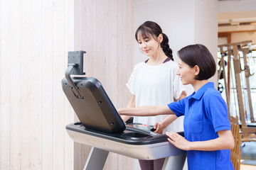 Obraz premium スポーツジムで運動する女性とトレーナー（ランニングマシン）