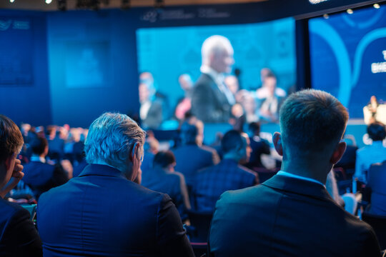 Businessmen Listening To Director Giving Presentation On Projection Screen At Export Forum