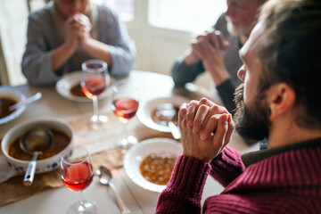 Multiethnic family saying prayer before eating meal at home together