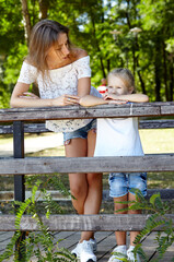 Fototapeta premium Mother and daughter walk in the summer city park. Childhood, leisure and people concept - happy family rest on nature and have a good time