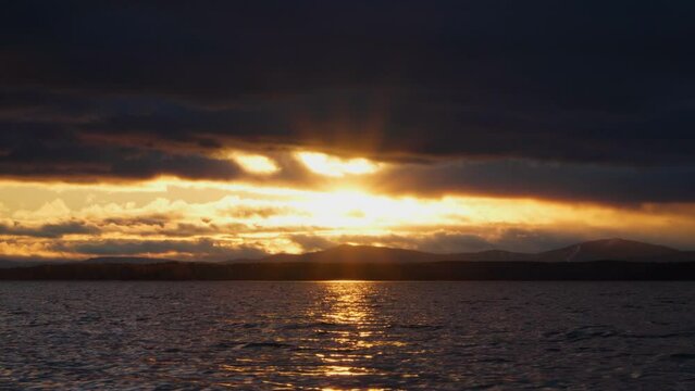 Gloomy cloudy sunset on the lake. The rays of the bright sun break through the dark clouds in the sky.