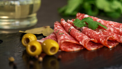 Fresh slices smoked sausage with spices and seasonings on stone board with olives. Cold cuts. Meat. Food