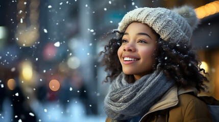 Mujer afroamericana de pie con gorro blanco de lana y sonriendo en un día que esta nevando en la ciudad. Mujer afroamericana sonriendo viendo caer nieve. - obrazy, fototapety, plakaty