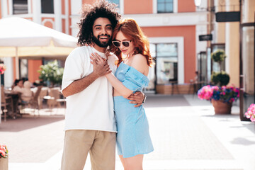 Smiling beautiful redhead  woman and her handsome boyfriend. Model in casual summer clothes. Happy cheerful family. Female having fun. Couple posing in the street at sunny day. In sunglasses