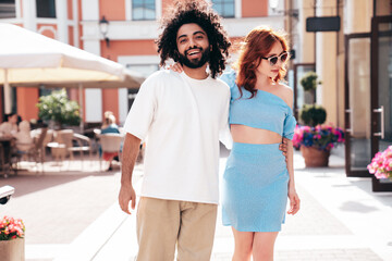 Smiling beautiful redhead  woman and her handsome boyfriend. Model in casual summer clothes. Happy cheerful family. Female having fun. Couple posing in the street at sunny day. In sunglasses
