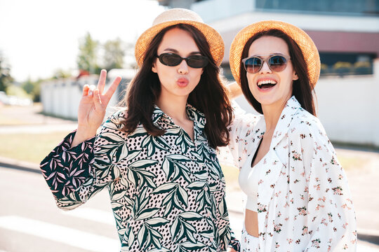 Two young beautiful smiling hipster female in trendy summer costumes  clothes. Sexy carefree women posing in the street. Positive models having fun at sunny day. Going crazy. In sunglasses and hat