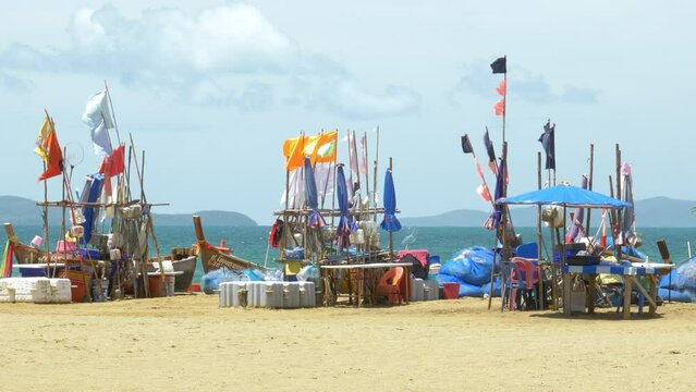 Colorful cloth banners on wooden poles blown by the wind on a beachfront alongside boats docked on the seashore.
