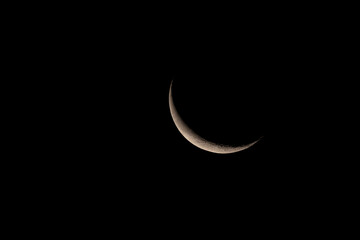 A narrow crescent of the waning moon in the night sky.