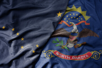 big waving colorful national flag of north dakota state and flag of alaska state .