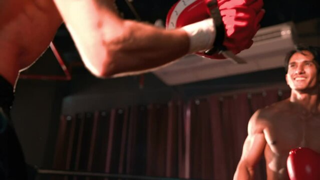 Asian and Caucasian Muay Thai boxer unleash punch in fierce boxing training session, delivering punching strike to sparring trainer, showcasing Muay Thai boxing technique and skill. Impetus
