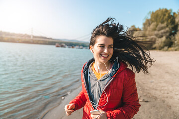 Young smiling woman running on the beach with the wind in her long hair. Beautiful woman doing her...