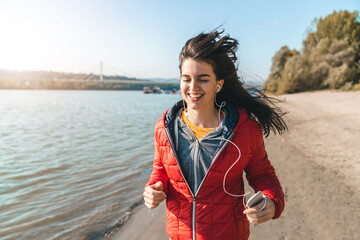 Beautiful young woman enjoying freedom while running on the beach during the sunny, but cold autumn...