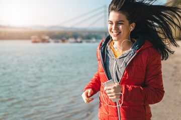 Young adult female enjoying fitness routine by listening to music and running outdoors during the...
