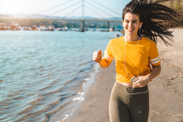 Attractive smiling female fitness instructor running by the seaside on a sunny day in autumn.