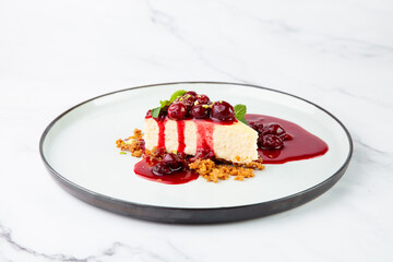 side view of cheesecake with juicy berries and mint on a white plate