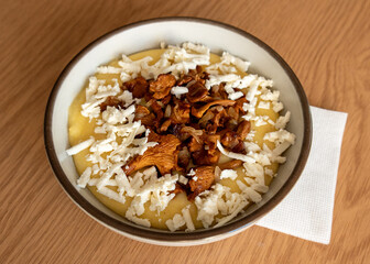 Tasty banosh served with brynza and mushrooms in bowl on table, top view. Traditional Ukrainian dish