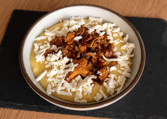 Tasty banosh served with brynza and mushrooms in bowl on table, top view. Traditional Ukrainian dish