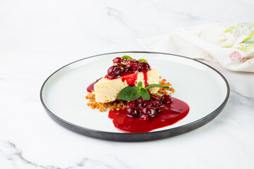side view of cheesecake with juicy berries and mint on a white plate