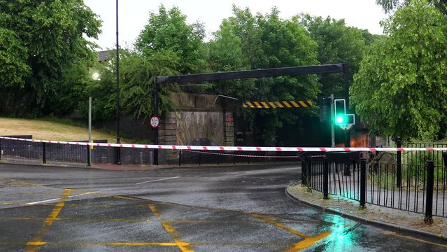 Road closed with Fire and Rescue Services tape. Heavy rain in summer. Traffic light, stoplight changing from green to red, no people or cars on the street.