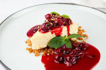side view of cheesecake with juicy berries and mint on a white plate