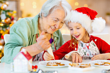 Grandmother and granddaughter prepare Christmas cookies and decorate them with icing for a happy...