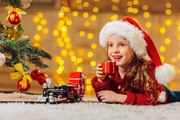 Portrait of a happy child in a Santa hat and a red sweater under a Christmas tree