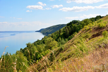 hillside with green trees and blue lake and clouds on sky copy space 