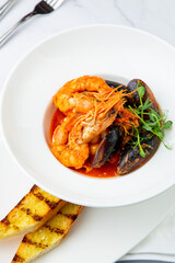 shrimp and mussels with herbs in a white plate with toasted bread, side view