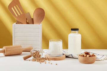 Front view of a milk cup placed on wooden podium, displayed with a bowl of nuts, soybeans, kitchen utensil and a milk bottle. Empty label bottle for product promotion