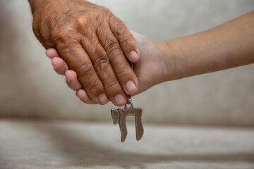 Am Israel Chai. Hands of an elderly man holding the hand of a child close up. they holding a silver Chai key chain, which spell "life" in Hebrew. Blurred background.
